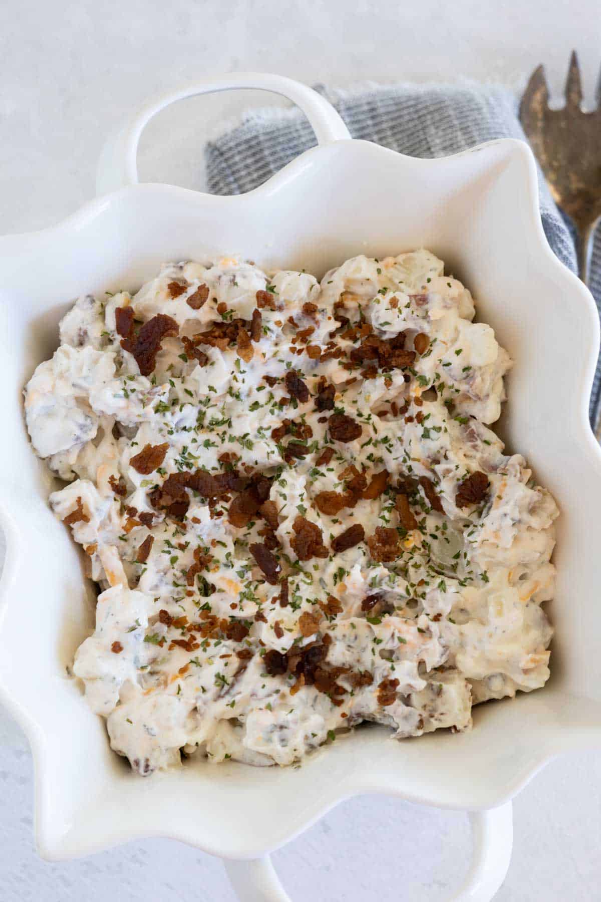 Red potato salad with cooked and crumbled bacon, grated cheddar cheese, and dill in a creamy dressing.