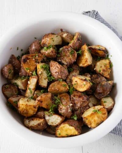 Golden brown roasted red potatoes with fresh parsley in a white serving bowl.