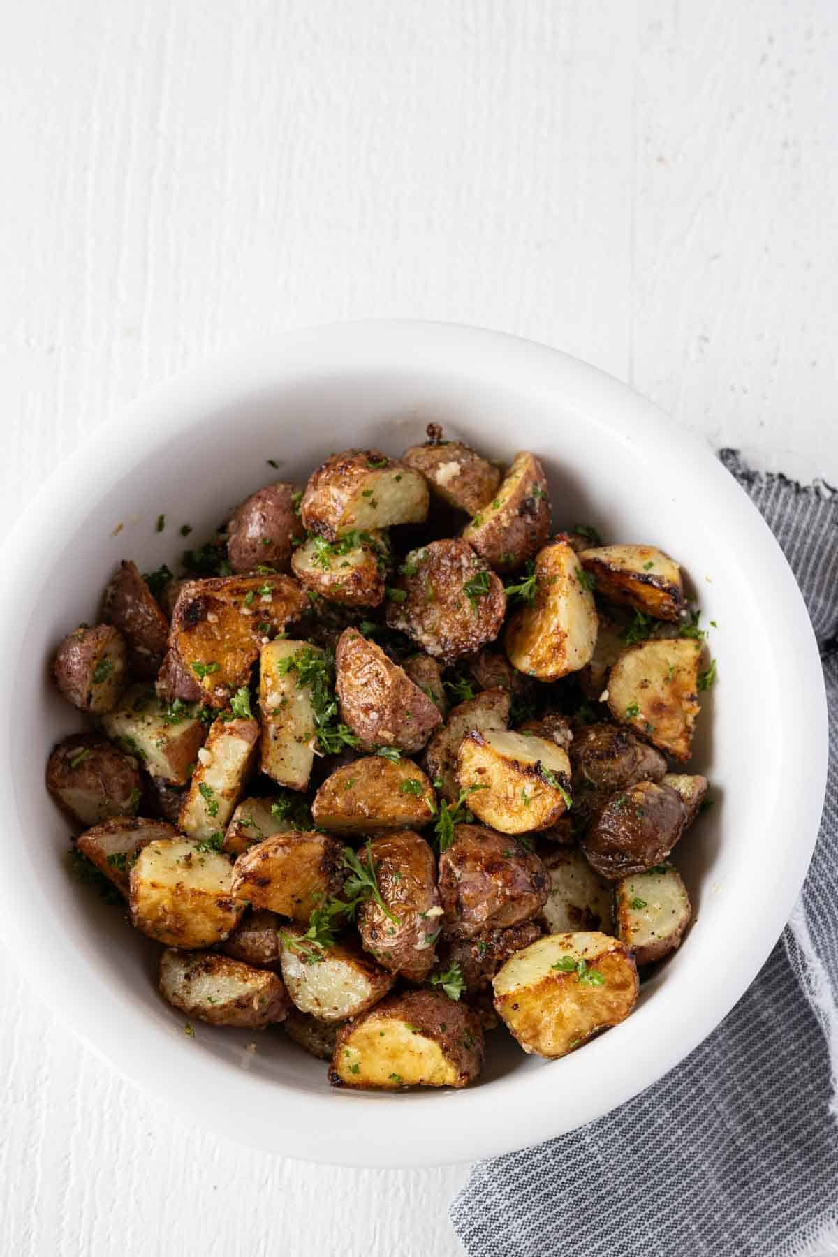 Golden brown roasted potatoes with parmesan and parsley in a white serving bowl.
