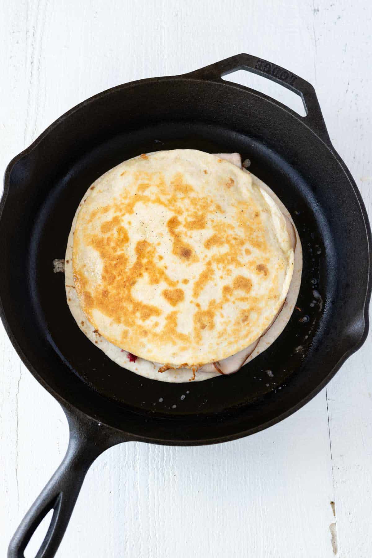 A golden brown fried quesadilla in a cast iron skillet.