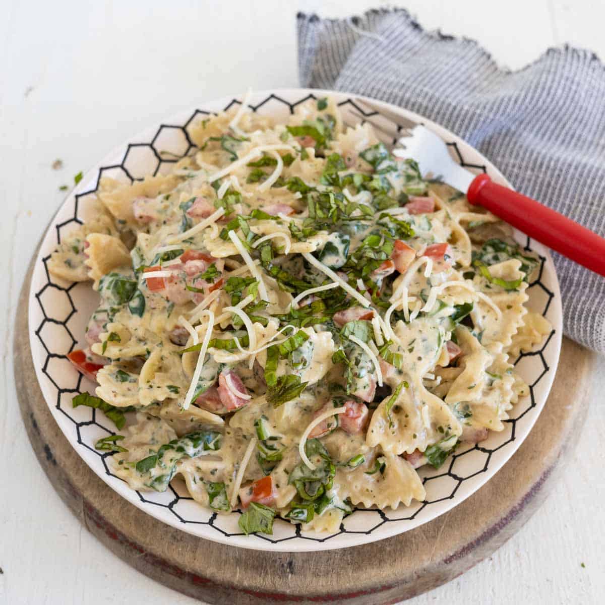 A plate with bowtie pasta with diced tomatoes and fresh spinach in a creamy sauce.