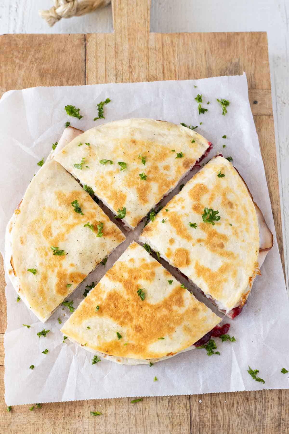 A quesadilla cut into wedges on a cutting board lined with parchment paper.